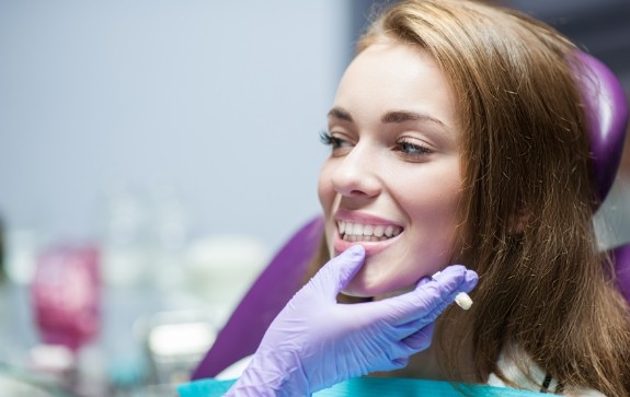 Dentist examining woman's smile after dental implant supported dental crown restoration
