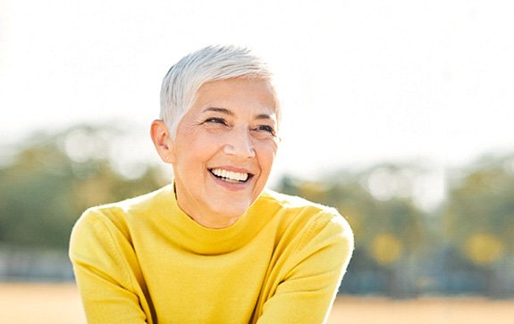 Senior woman in yellow sweater sitting outside smiling
