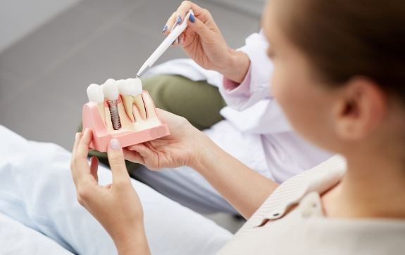 Dentist and patient looking at model comparing natural teeth and dental implant supported teeth