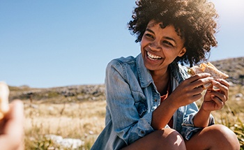 Woman smiling while eating sandwich outside
