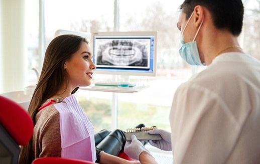 Dentist showing sample veneers to patient in front of X-ray image